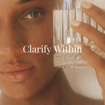 A close-up of a woman’s face with dewy skin, soft natural makeup, and clear blue-green eyes. She gently holds a faceted glass of water beside her cheek. The words “Clarify Within” appear in elegant white serif font.